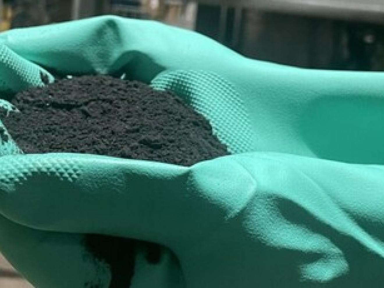 Two hands in green gloves hold a pile of black powder.