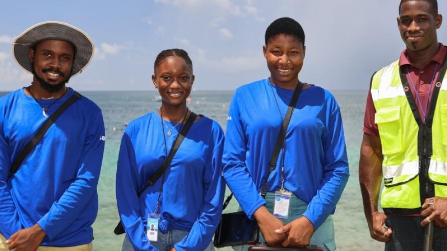 Four people in working gear standing on the beach with the ocean in the background look directly into the camera.