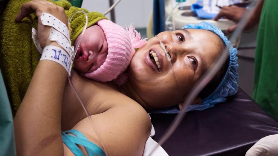 A person lying in a hospital bed with a baby.