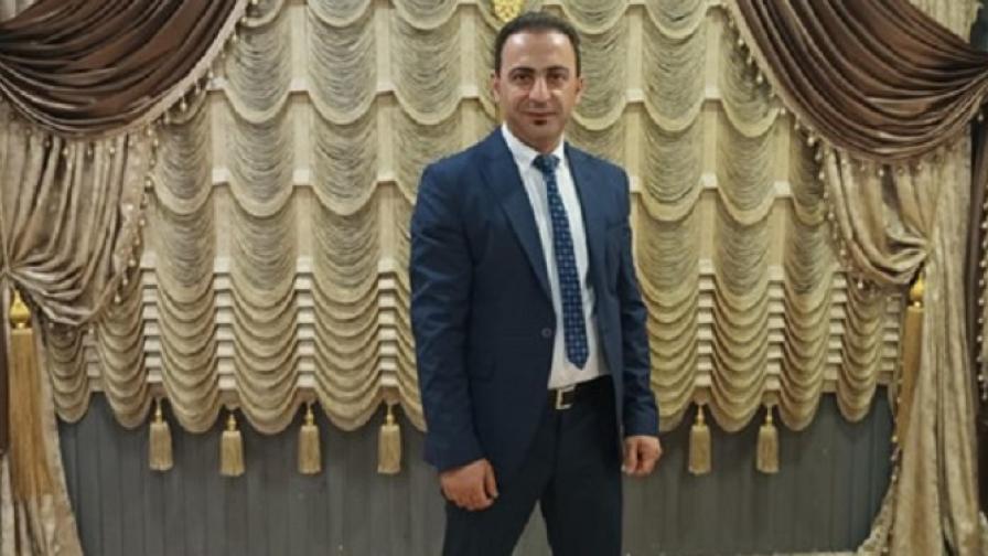 Ein Mann in einem Anzug mit Krawatte steht vor einer kunstvoll gerafften Vorhanginstallation in Gold-, Beige- und Brauntönen.