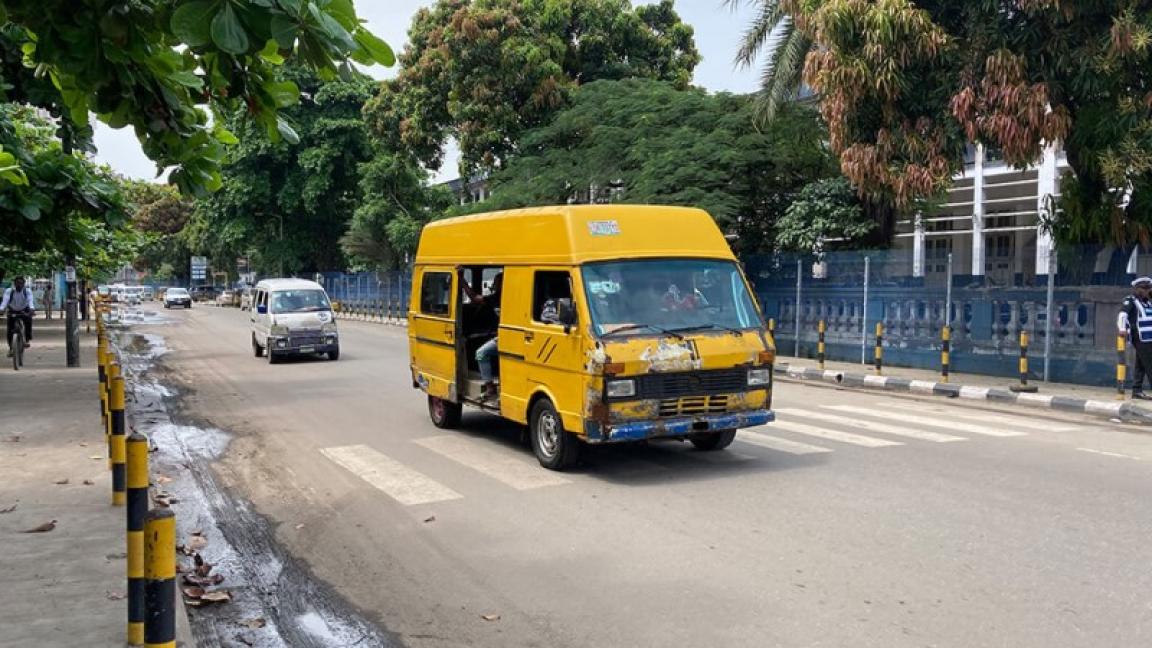 Ein gelber Bus fährt die Straße entlang, umgeben von städtischer Umgebung und Passanten.