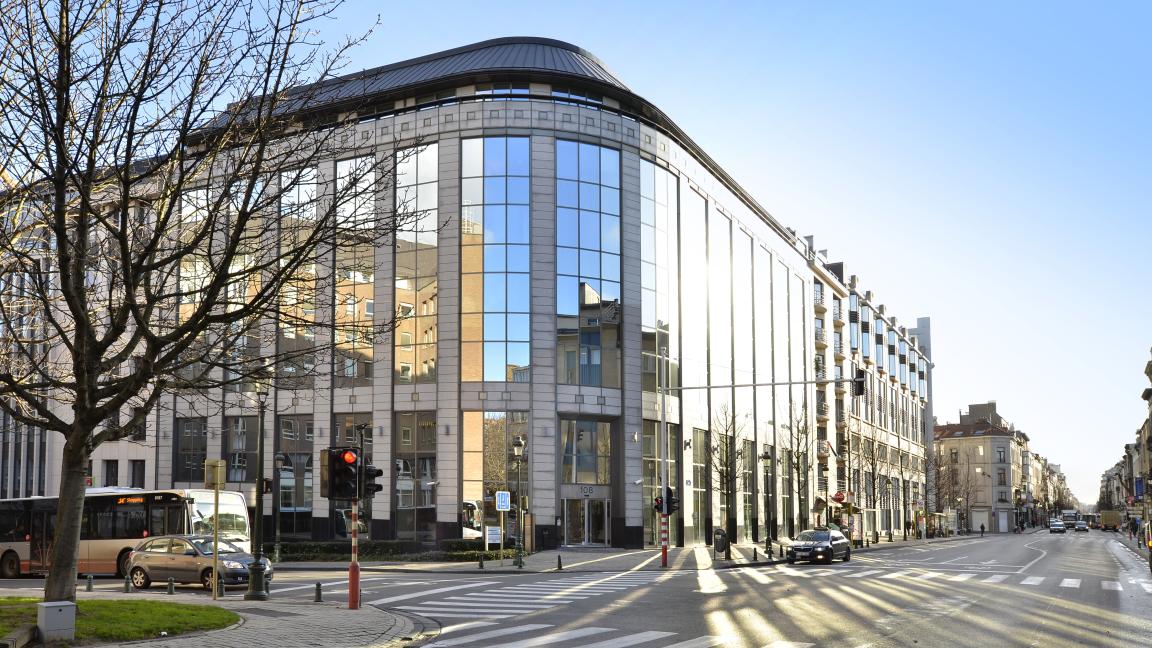 Außenansicht eines modernen Eckgebäudes mit vielen Fenstern an einer Straßenkreuzung.