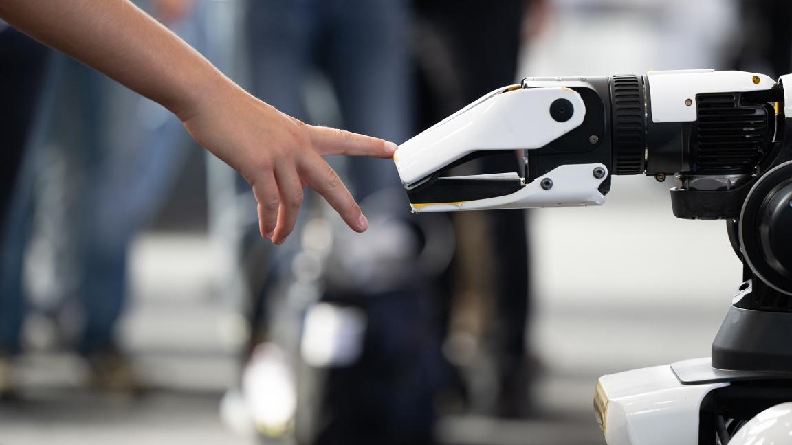 A human hand and a robotic hand almost touch, symbolizing the interaction between humans and technology.