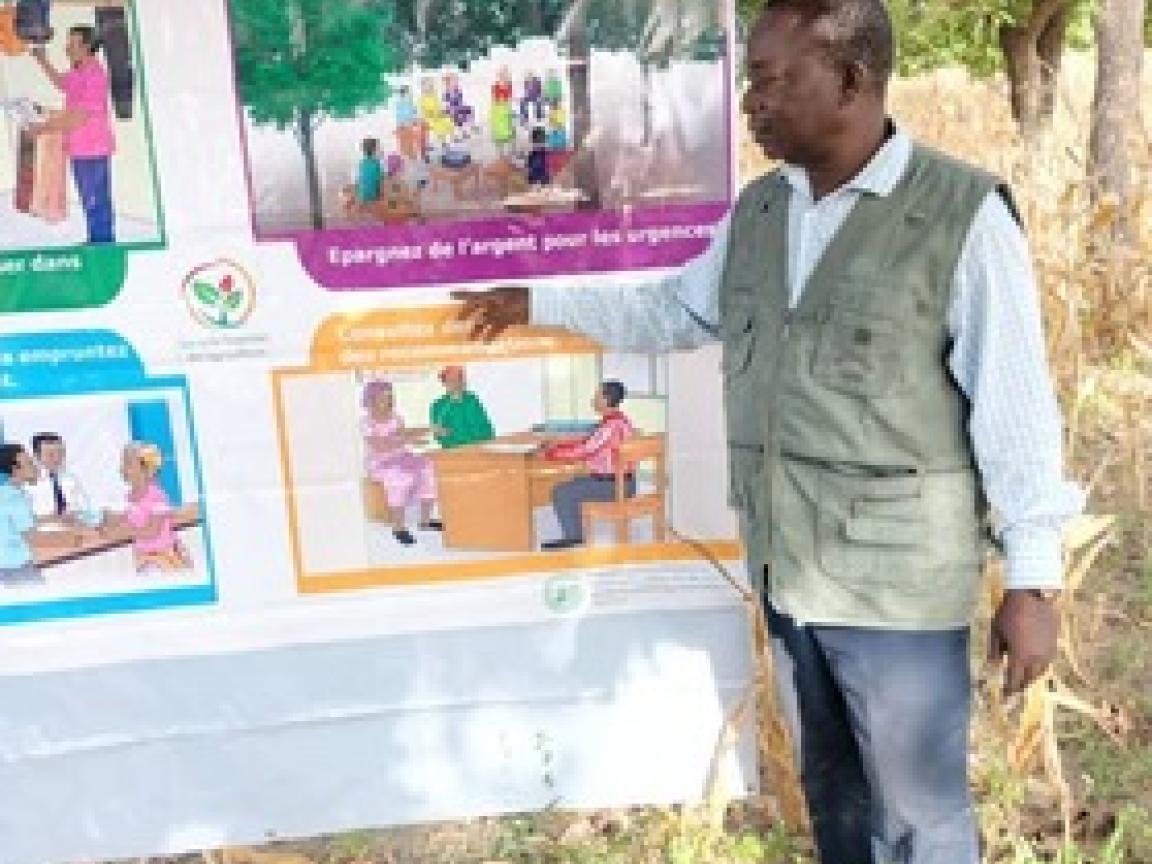 Ein Mann, der auf einem Plakat, dass unter einem Baum aufgespannt ist, etwas zeigt.