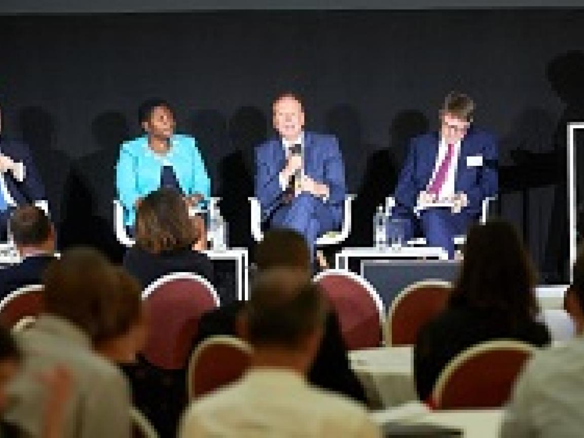 Vier Personen sitzen auf Stühlen nebeneinander auf einer Bühne