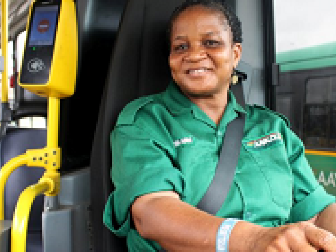 Frau in einem grünen Oberteil sitzt auf dem Fahrersitz in einem Bus