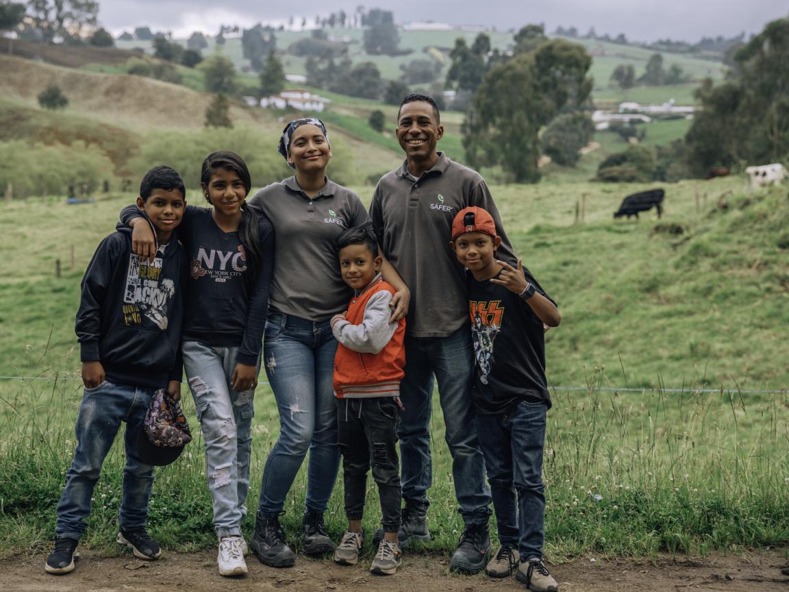 Zwei Erwachsene und vier Kinder stehen Arm in Arm in einer Landschaft mit grünen Hügeln