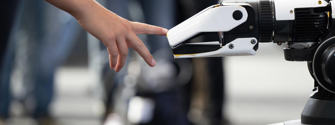 A human hand and a robotic hand almost touch, symbolizing the interaction between humans and technology.