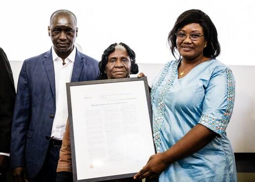 Drei Personen vor einer Wand, eine davon hält einen Bilderrahmen in der Hand