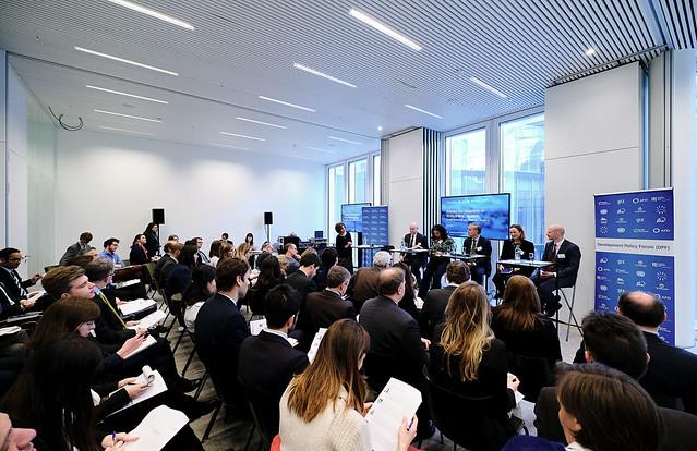 5 Personen sitzen auf Stühlen auf einer Bühne und reden zu einem Publikum