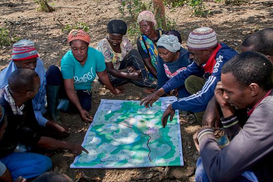 Viele Menschen sitzen auf dem Boden um eine Karte herum