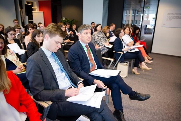 Personen sitzen nebeneinander auf Stühlen und haben ein Blatt Papier in der Hand