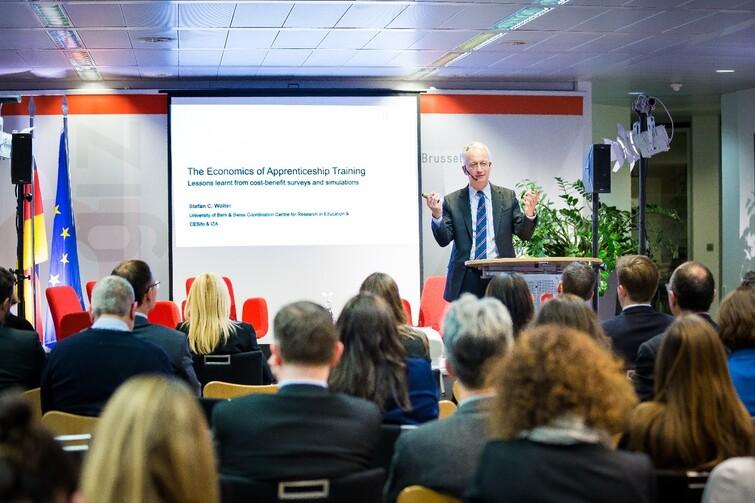 Mann steht auf einer Bühne und redet zu einem Publikum