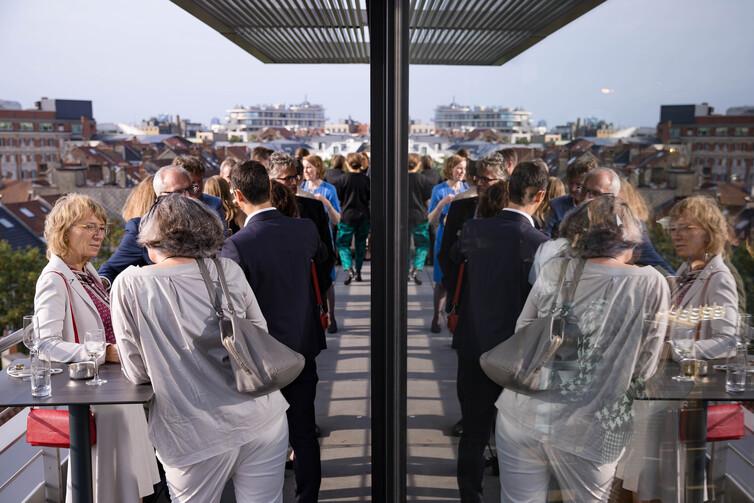 Viele Personen stehen draußen auf einem Balkon und unterhalten sich