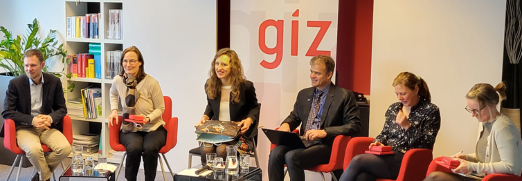 Mehrere Personen sitzen auf roten Stühlen in einem halb Kreis