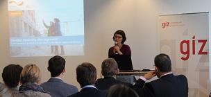 Person steht auf einer Bühne mit einem Mikrofon in der Hand vor Publikum