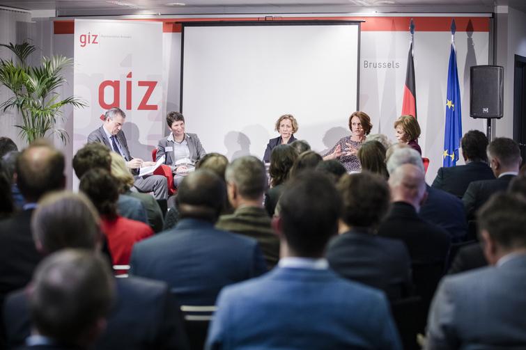 Mehrere Personen sitzen auf roten Stühlen in einem halb Kreis