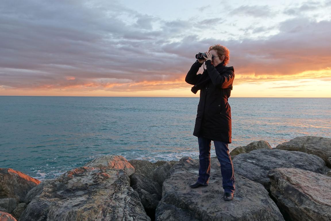 Woman standing on rocky coast looking through binoculars
