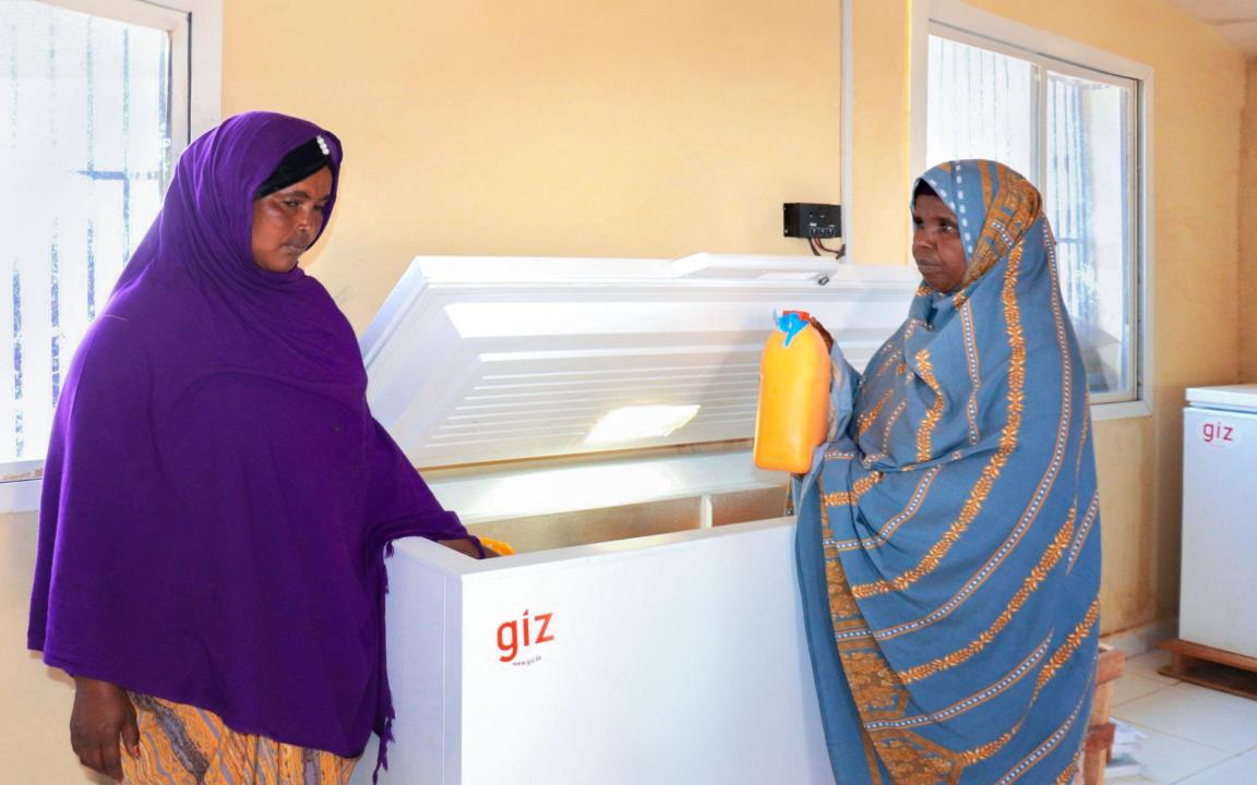Two women are standing at a freezer cabinet, one of them is holding a milk container in her hand.