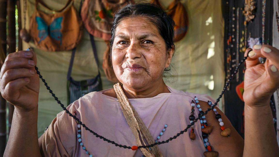 An indigenous woman holds a handmade necklace in front of the camera.