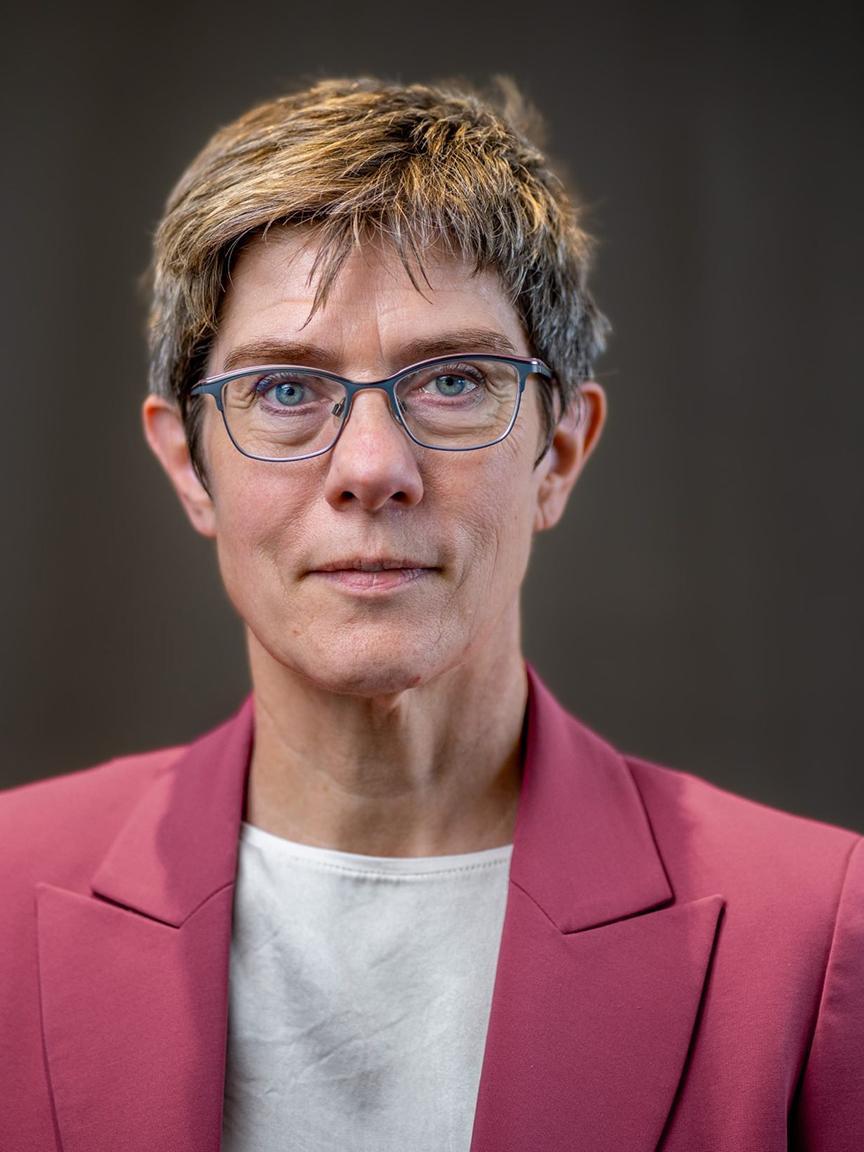 Portrait of a middle-aged woman with short, highlighted hair, glasses, a white top and a red blazer in front of a neutral background, looking directly into the camera.