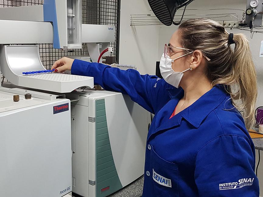 A woman wearing blue protective clothing and a mask operates a scientific analysis device in the laboratory.