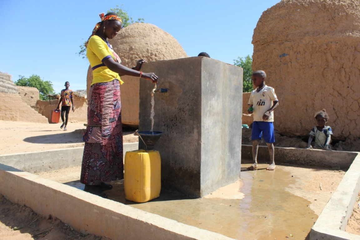 A woman fills a canister with water at a well.