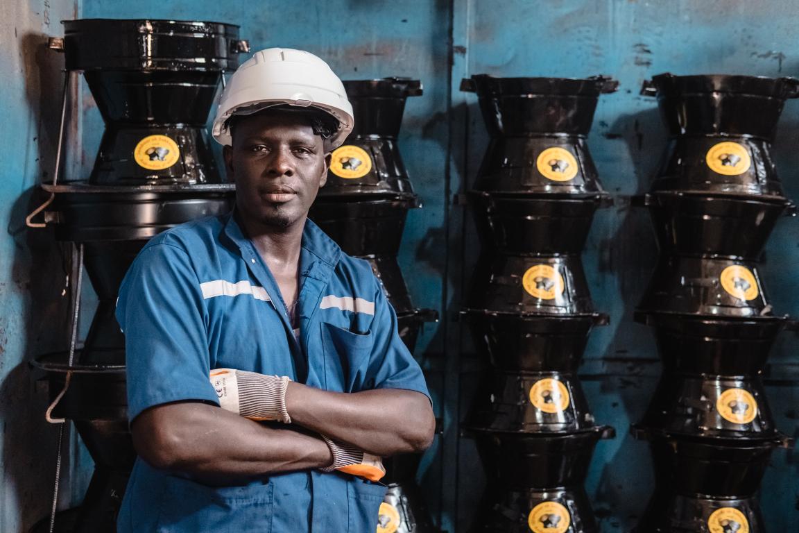 A man in a white helmet stands in front of a wall where cookers are piled up.