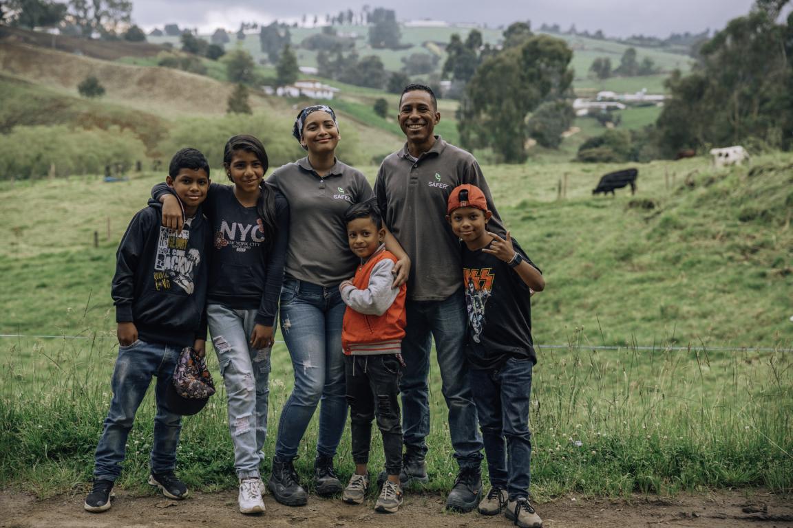 Zwei Erwachsene und vier Kinder stehen Arm in Arm in einer Landschaft mit grünen Hügeln