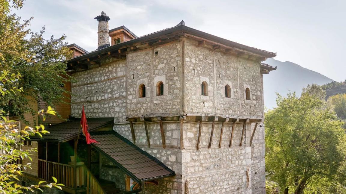 A historic stone building with small windows and a wooden roof in a green setting.