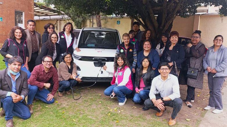 A group of people standing in front of an electric car during a training session on electric mobility