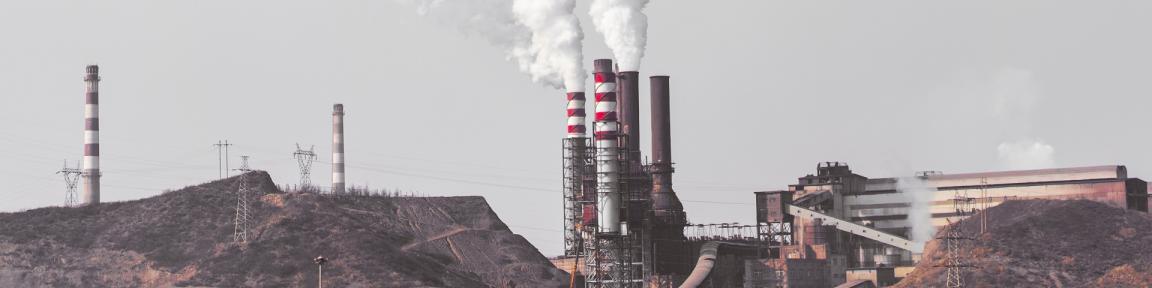 Schornsteine einer Industrieanlage stoßen weißen Rauch in den Himmel.