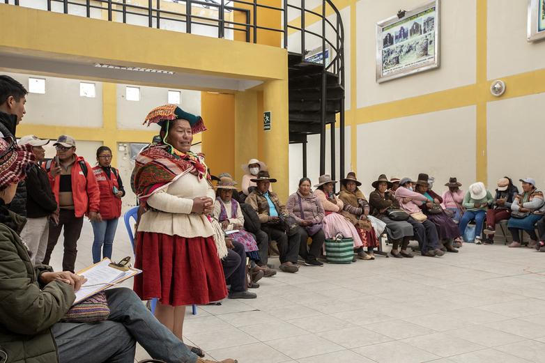 Artesanos y artesanas sentados y de pie asistiendo a una reunión en una sala.