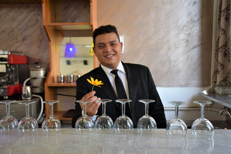 Un jeune homme se tient derrière le comptoir d'un restaurant et tient une fleur.
