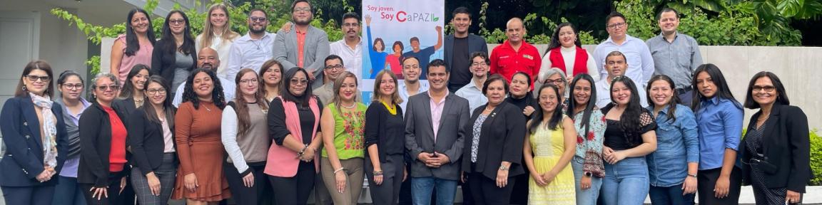 Participantes del proyecto posan de pie para fotografiarse junto a un expositor del proyecto.