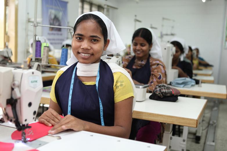 A woman smiles while using a sewing machine.
