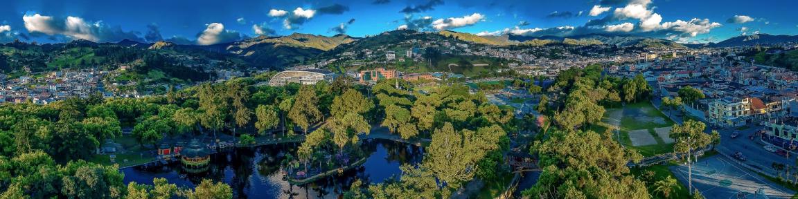 Imagen panorámica de un parque alrededor del cual se extienden una ciudad verde y un paisaje de colinas.