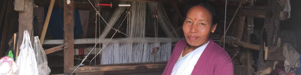 Eine Frau steht vor einem Webstuhl aus Holz.