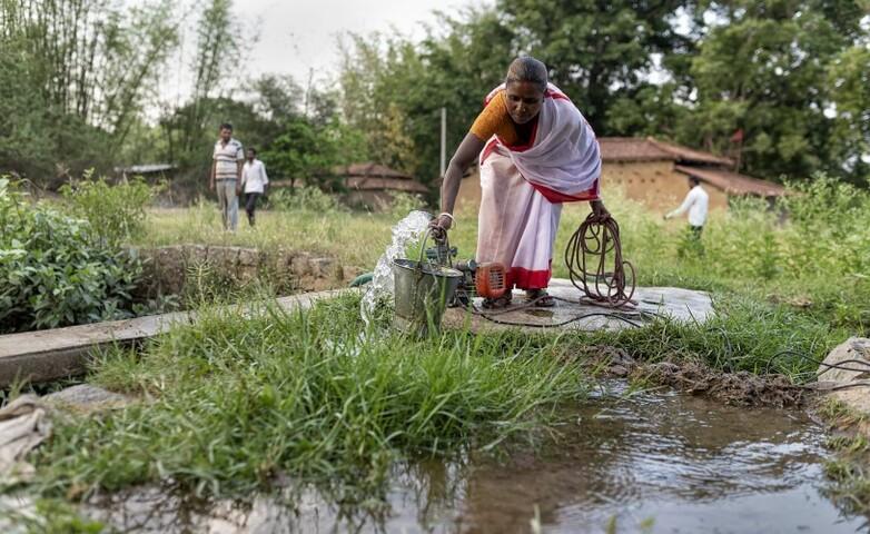 A person drawing water from a pump into a container in a rural area.
