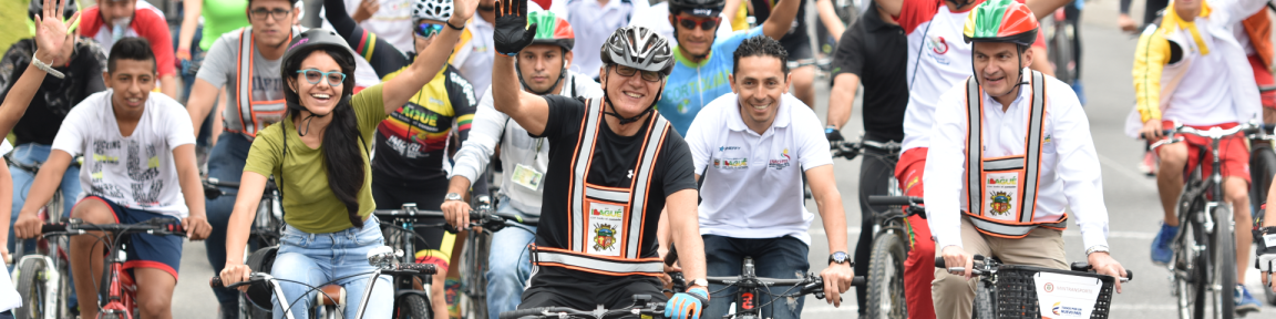 Numerosos ciclistas circulan juntos al lado y detrás unos de otros por una calle.