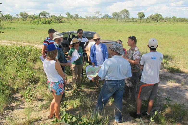 A group of people standing at the edge of a field; some are holding maps.