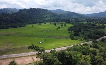 Landscape of Hin Nam No National Protected Area in Lao PDR, featuring green fields, forested hills, and a road cutting through the scenery.