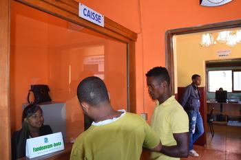 Two men stand in front of a woman at an administration counter.