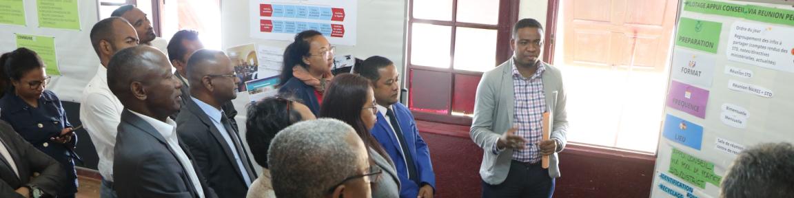 Menschen stehen vor einer Präsentationswand, ein Mann spricht.