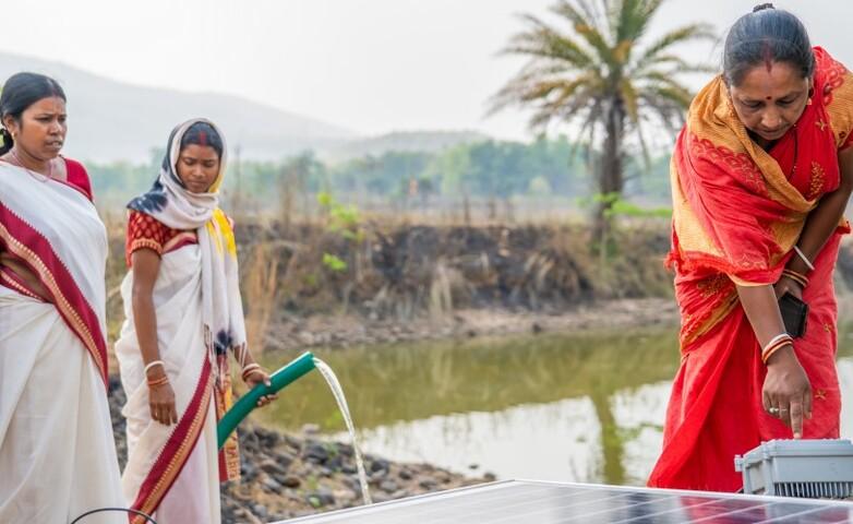 Women operating a solar-powered water pump near a pond in a rural area in India.
