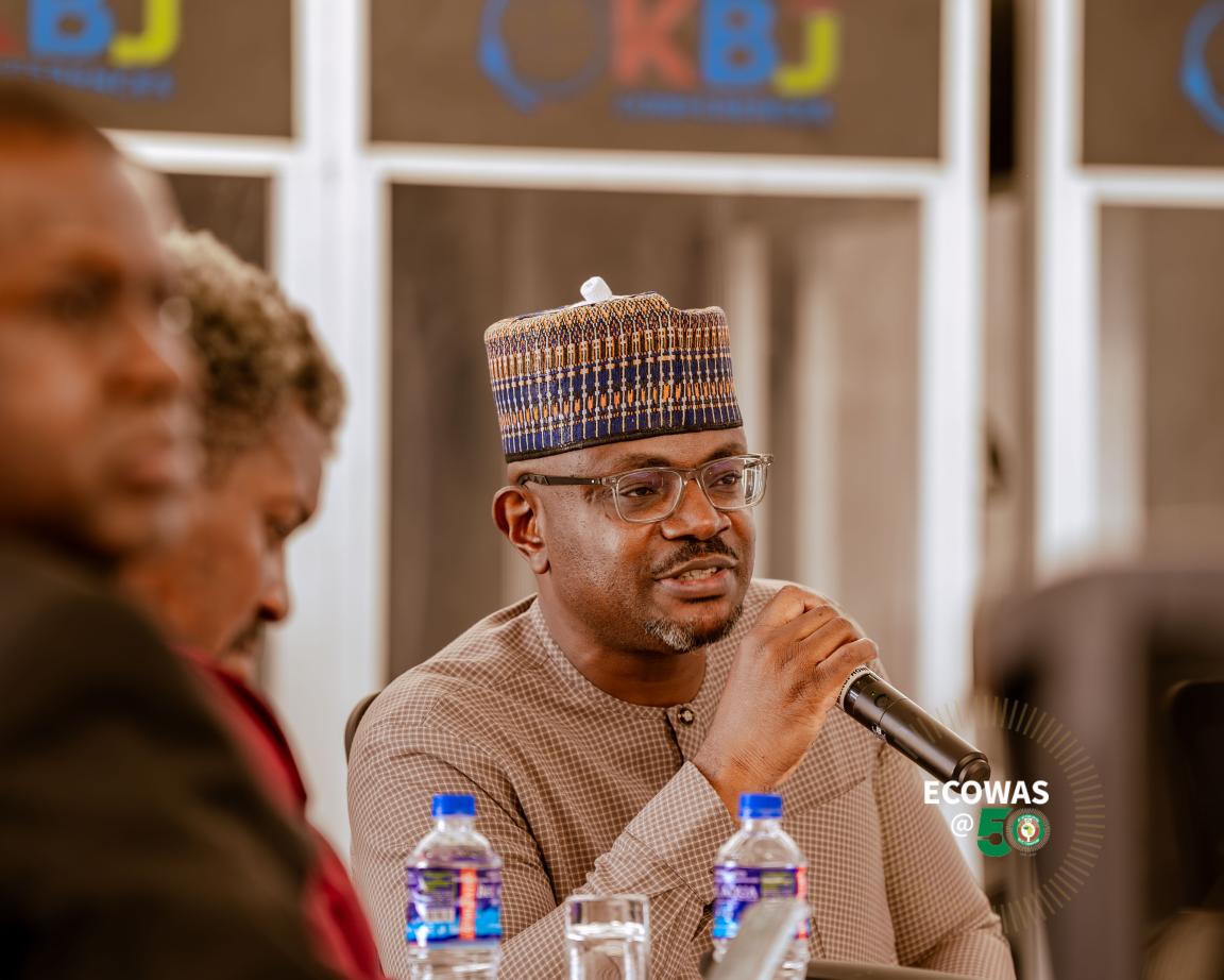 Eine Person mit Hut und Brille spricht in ein Mikrofon.