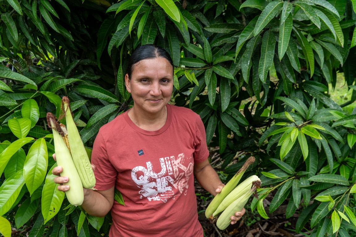 Eine Frau steht vor einem Baum und hält Bananen in der Hand.