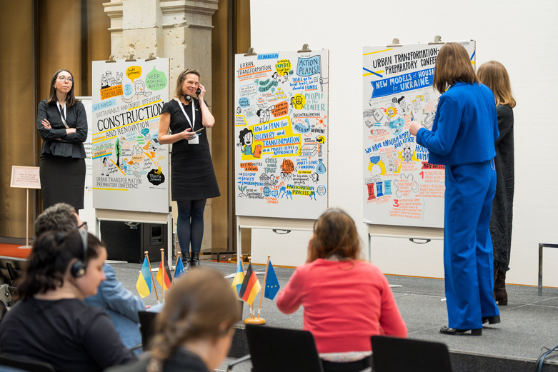 Frauen präsentieren auf einer Bühne die Konferenzergebnisse in Illustrationen.