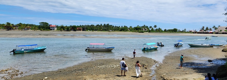 Am Strand von Portete in Ecuador ankern Boote im Wasser und Menschen laufen am Ufer entlang. 