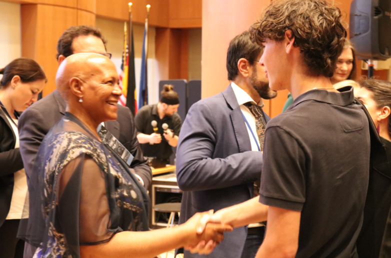 Botschafterin Nosipho Nausca-Jean Jezile schüttelt einem jungen Teilnehmenden beim deutschen HLPF-Side-Event die Hand.